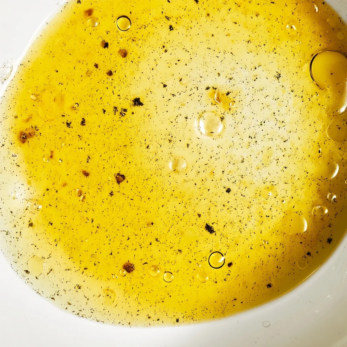 Golden homemade easy lemon vinaigrette dressing drizzled over fresh green salad with lemon wedge