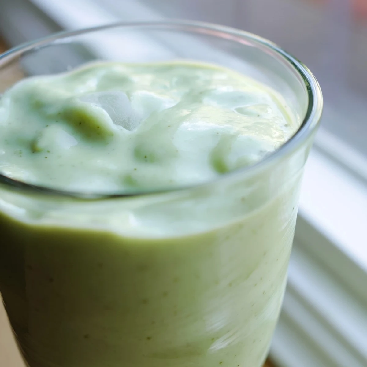 Thick green Greek yogurt avocado smoothie topped with fresh banana slices
