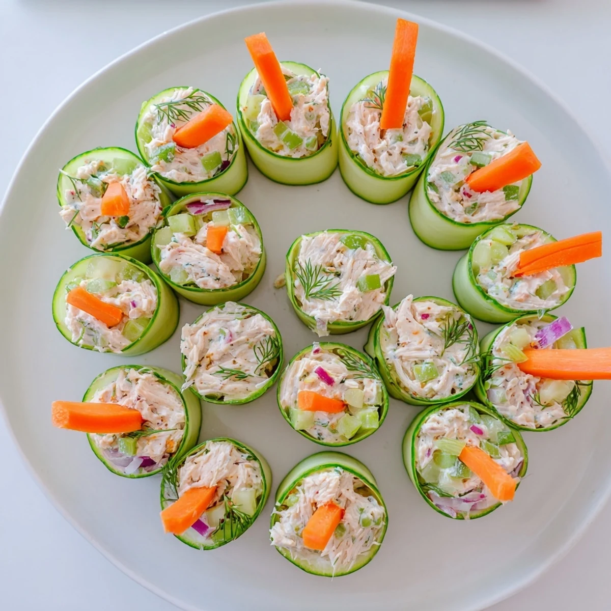 Fresh chicken salad cucumber roll ups arranged on a white serving platter with dill garnish