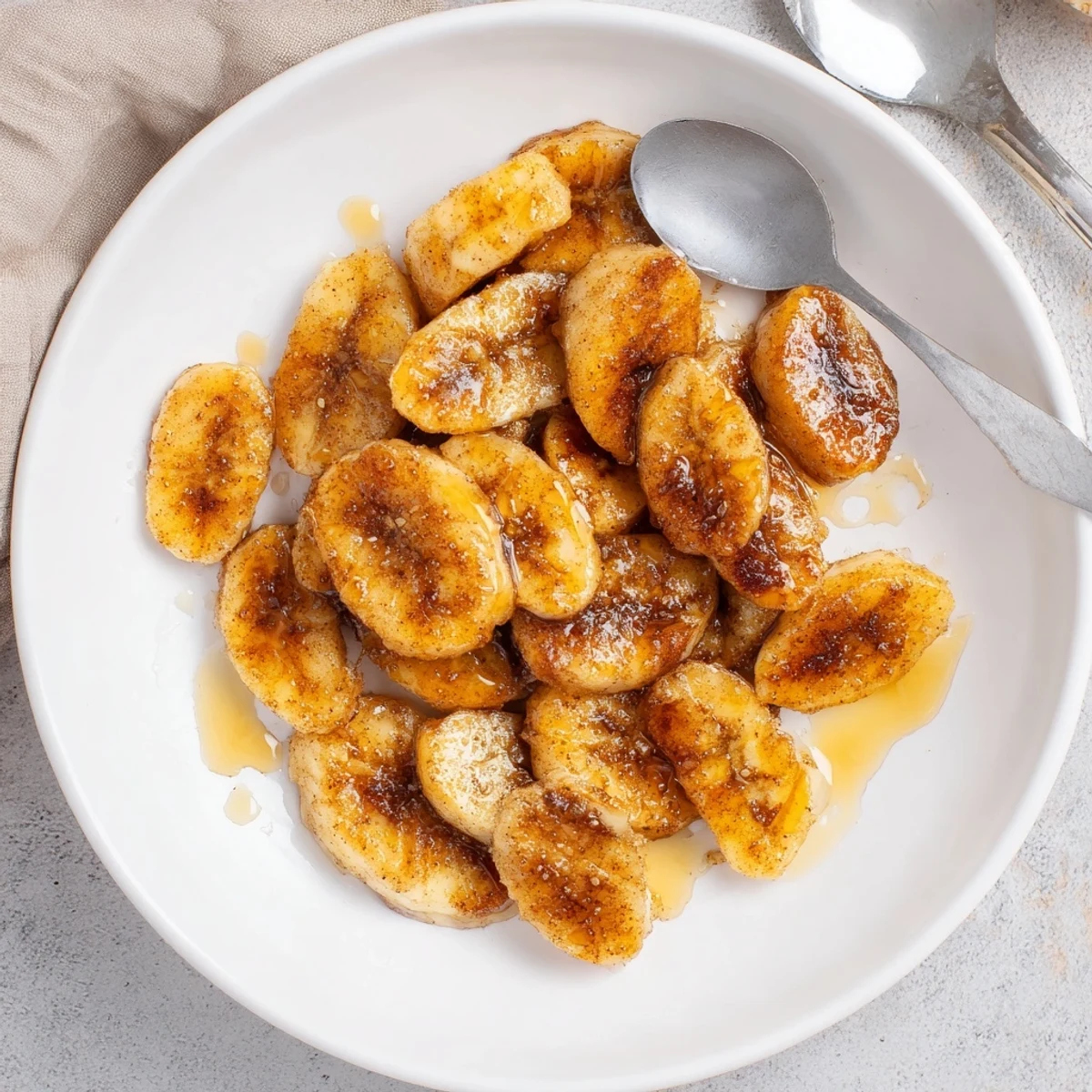Warm caramelized pan fried cinnamon bananas arranged on a white plate