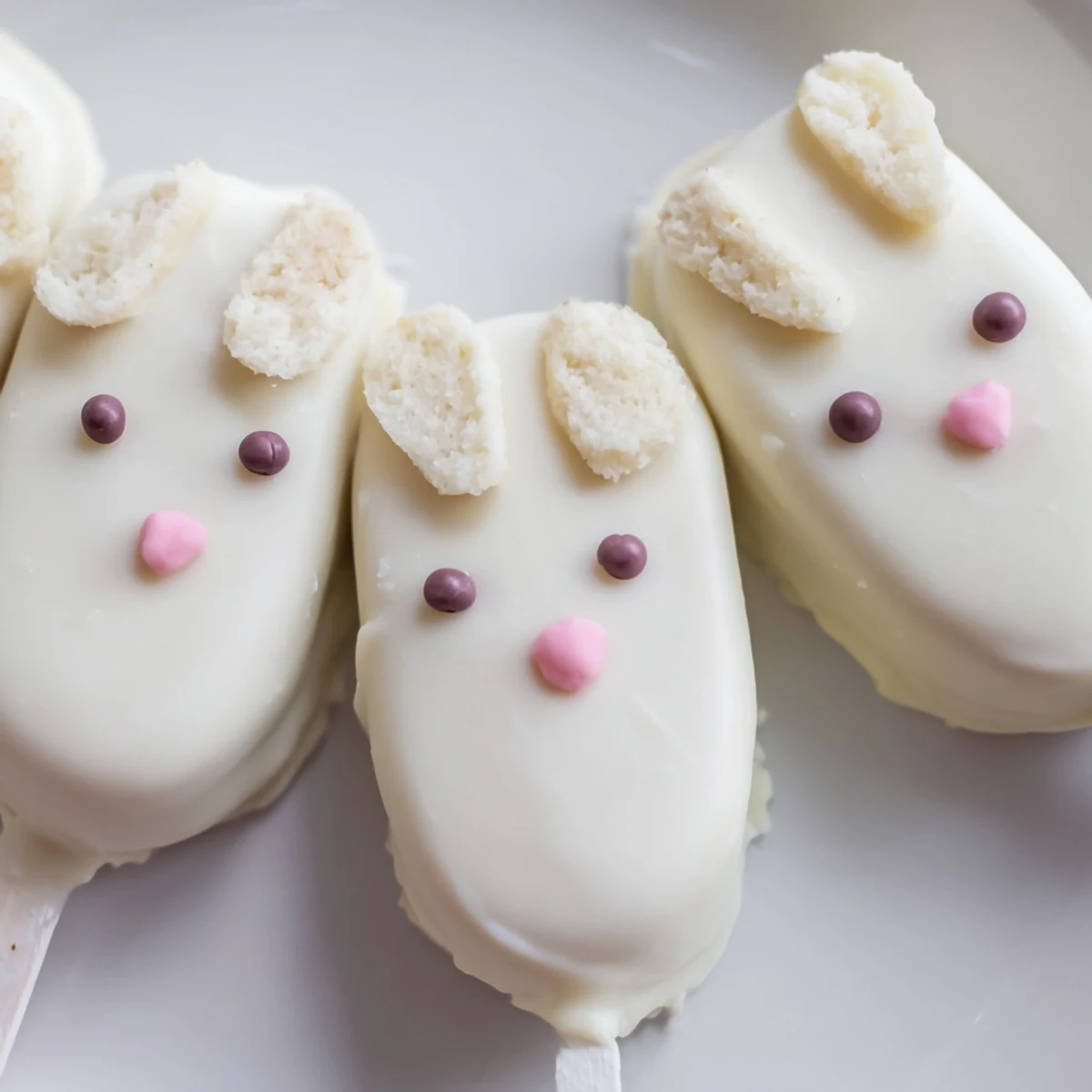 Homemade white chocolate bunny cakesicles displayed on parchment with colorful fondant decorations