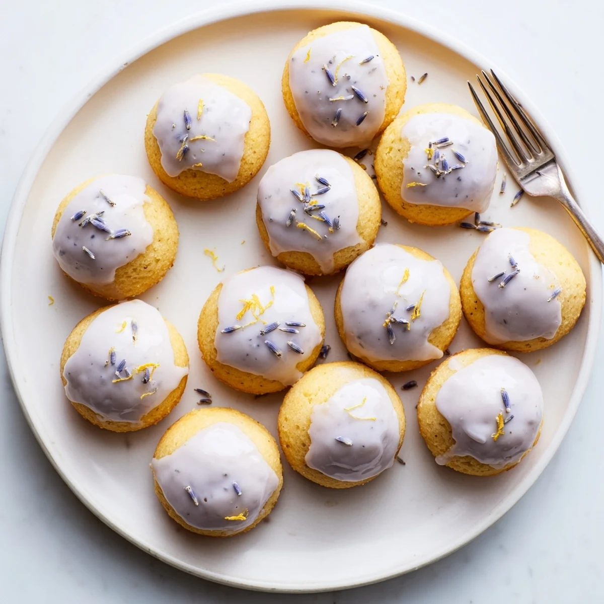 Drizzled mini lemon cakes with lavender glaze served on a delicate tea saucer