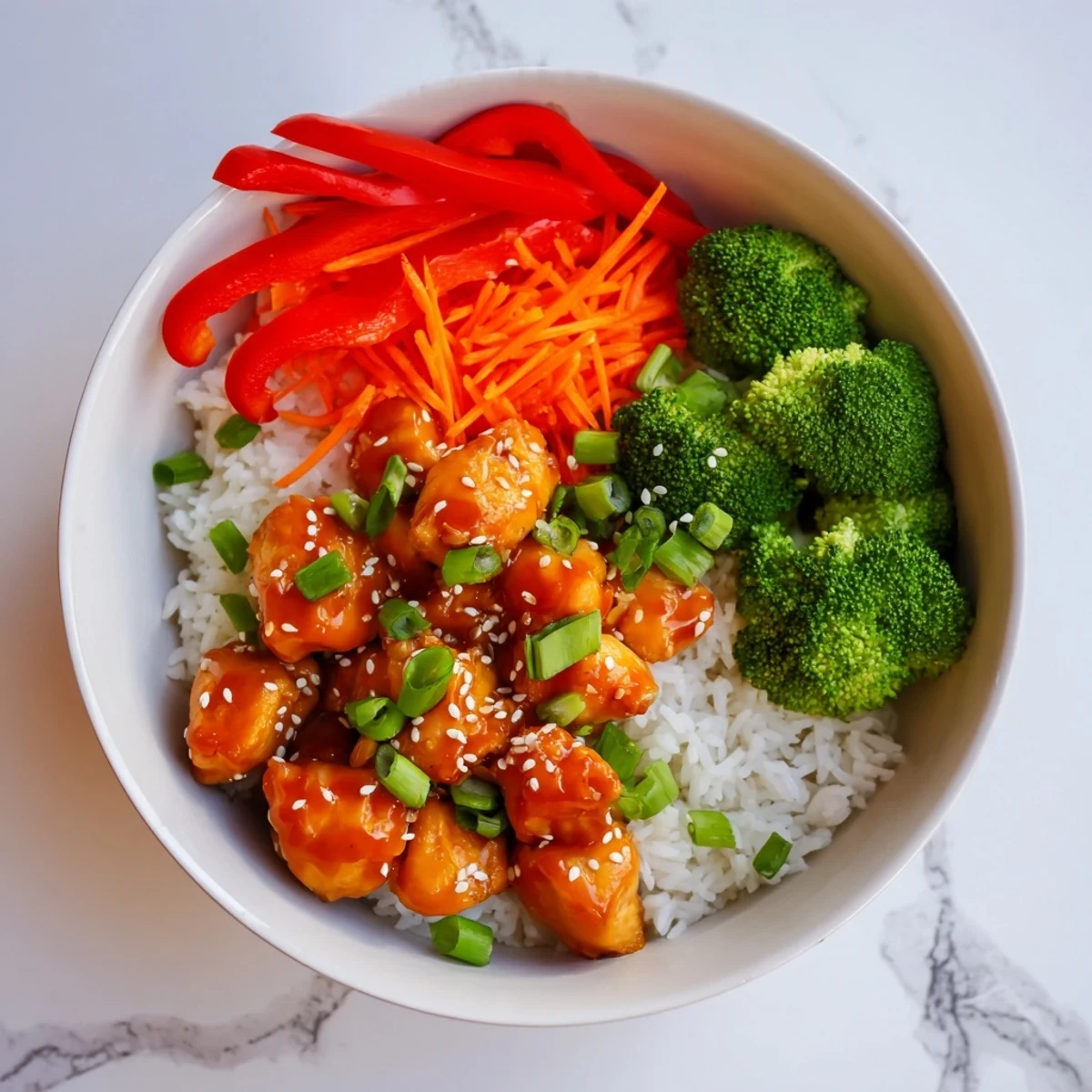Golden orange glazed chicken pieces atop fluffy white rice with vibrant broccoli and shredded carrots