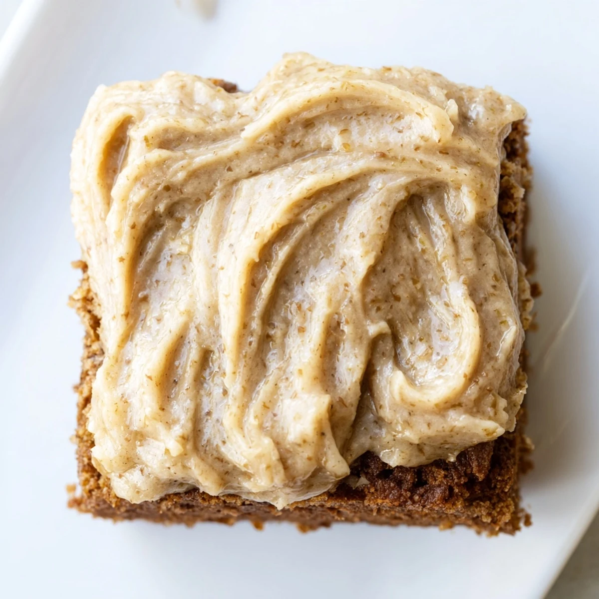 Golden brown banana bread brownies topped with creamy brown butter frosting on a white plate