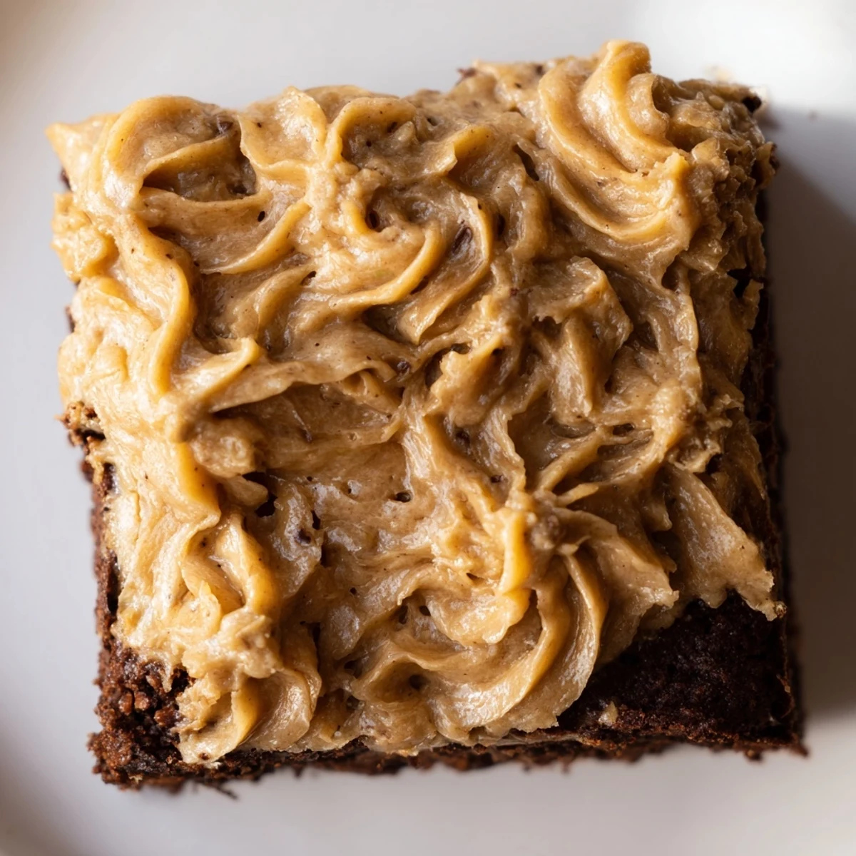 Thick frosted banana bread brownie squares sprinkled with powdered sugar on a rustic wooden board