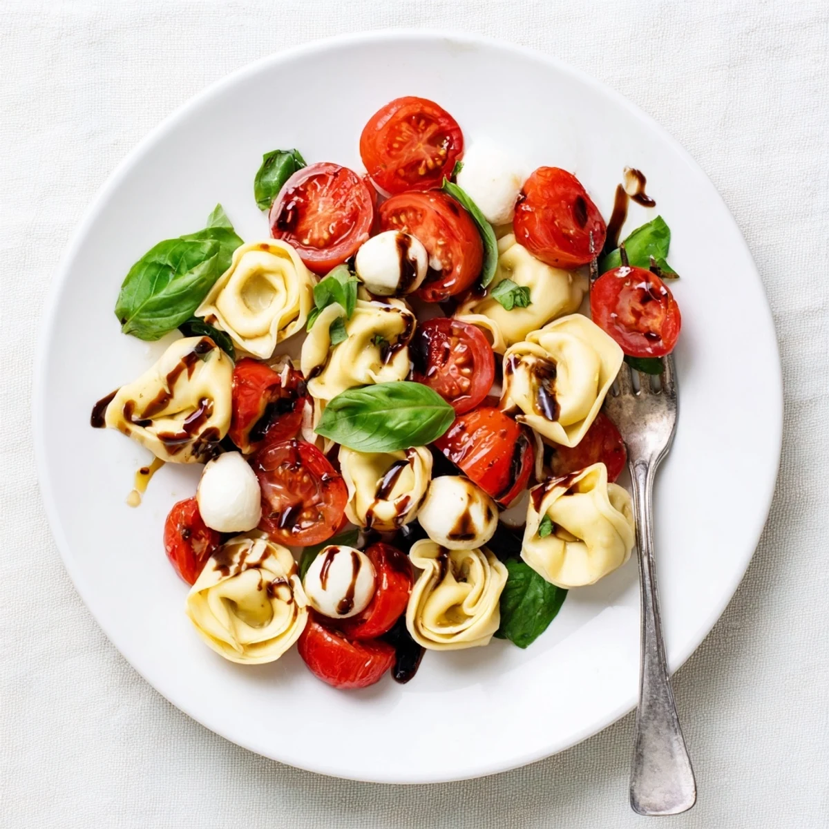 Colorful bowl of tortellini caprese salad with cherry tomatoes, fresh basil, and mozzarella drizzled with balsamic glaze
