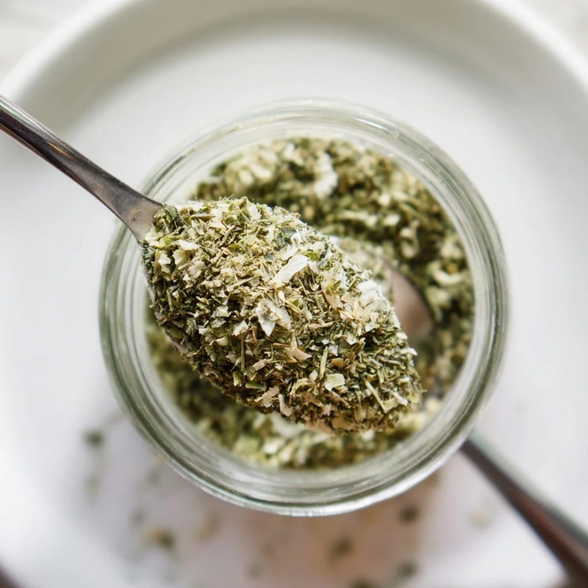 Handfuls of dried herbs being blended into Dehydrated Tzatziki Seasoning Mix inside a shallow ceramic mixing bowl